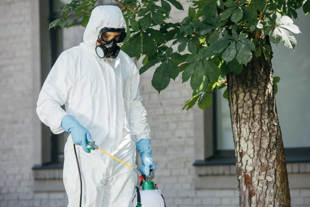 Homem utilizando equipamento de proteção enquanto dedetiza a área externa de uma empresa